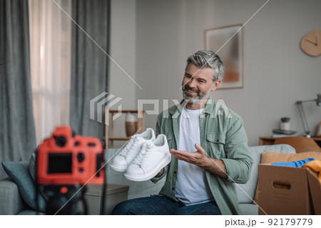Cheerful elderly european man blogger with beard records video review on shoes, unpacks purchases 92179779