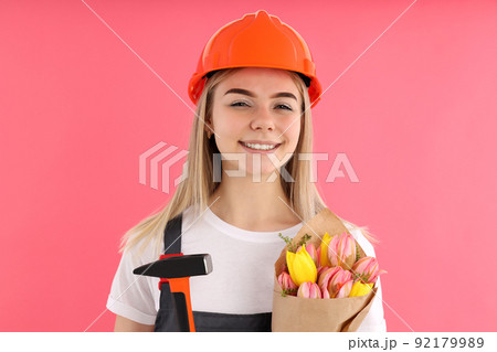 Builder girl with bouquet of flowers on pink background Builder girl with bouquet of flowers on pink background 92179989