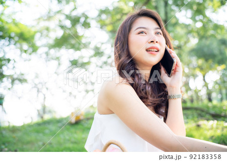 Cheerful young woman talking smartphone in city green park Cheerful young woman talking smartphone in city green park 92183358