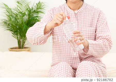 パジャマを着て寝室でペットボトルの水を飲むミドル女性 92186702