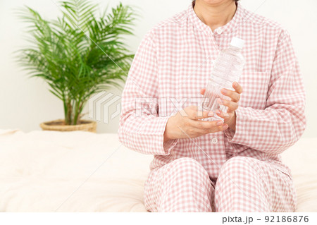 パジャマを着て寝室でペットボトルの水を飲むミドル女性 92186876