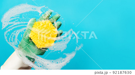 Banner of cleanup. A hand in rubber gloves wipes the glass with a foam sponge. Blue background with copy space. The concept of professional cleaning service Banner of cleanup. A hand in rubber gloves wipes the glass with a foam sponge. Blue background with copy space. The concept of professional cleaning service 92187630
