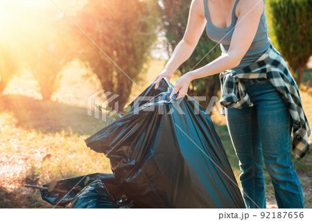 The concept of environmental pollution and Earth Day. A female volunteer does cleaning in the Park in front of the house, stacking bags of garbage. Close up The concept of environmental pollution and Earth Day. A female volunteer does cleaning in the Park in front of the house, stacking bags of garbage. Close up 92187656