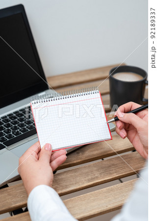 Businesswoman Holding Pen And Notepad With Important Message On Table With Lap Top And Coffee. Woman Presenting Crutial Information On Paper On Desk With Computer And Cup. 92189337
