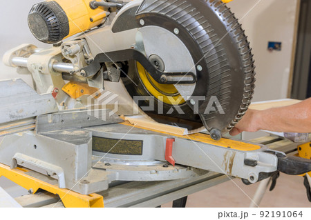 Using a miter saw, a construction worker cuts wood moldings for baseboards during the finishing process Using a miter saw, a construction worker cuts wood moldings for baseboards during the finishing process 92191064