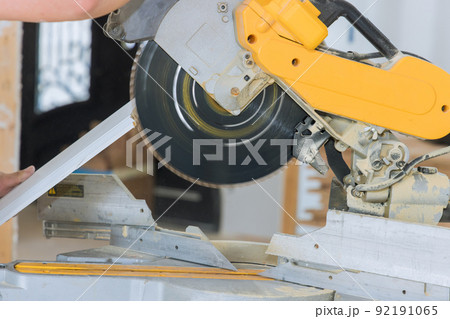 Construction workers are cutting wood moldings baseboards on the circular saw for the finishing work on the construction projects 92191065