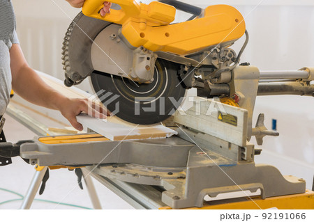 Construction worker cuts wood moldings baseboard on the miter saw 92191066