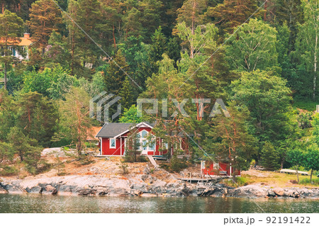 Sweden. Beautiful Red ASwedish Wooden Log Cabins Houses On Rocky Island Coast In Summer. Lake Or River Landscape 92191422