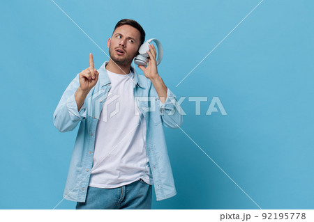 Thoughtful pensive tanned handsome man in casual basic t-shirt hold listen headphones look point finger up posing isolated on blue studio background. Copy space Banner Mockup. Music concept Thoughtful pensive tanned handsome man in casual basic t-shirt hold listen headphones look point finger up posing isolated on blue studio background. Copy space Banner Mockup. Music concept 92195778