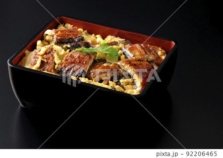 鰻の蒲焼きを卵でとじて三つ葉を乗せた鰻玉重を黒背景で撮影 92206465