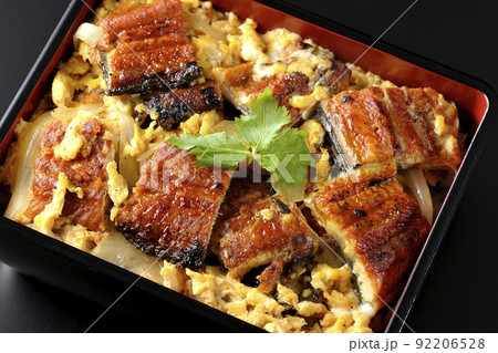 鰻の蒲焼きを卵でとじて三つ葉を乗せた鰻玉重を黒背景で俯瞰撮影 92206528