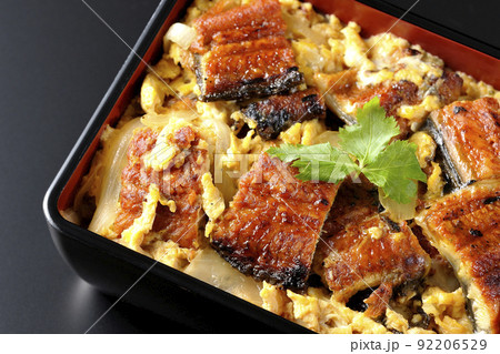 鰻の蒲焼きを卵でとじて三つ葉を乗せた鰻玉重を黒背景で俯瞰撮影 92206529