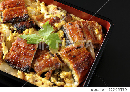 鰻の蒲焼きを卵でとじて三つ葉を乗せた鰻玉重を黒背景で俯瞰撮影 92206530