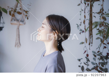明るい植物のある室内で目を瞑るワンピース姿の日本人女性 92207963