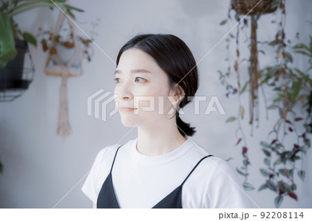 明るい植物のある室内でどこかを見つめるワンピース姿の日本人女性 92208114