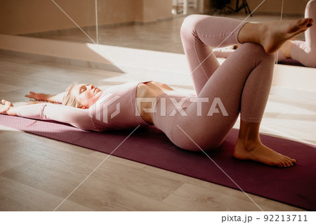 Young sporty woman, fitness instructor in pink sportswear doing stretching and pilates on yoga mat in the studio with mirror. Female fitness yoga routine concept. Healthy lifestyle and harmony. Young sporty woman, fitness instructor in pink sportswear doing stretching and pilates on yoga mat in the studio with mirror. Female fitness yoga routine concept. Healthy lifestyle and harmony. 92213711