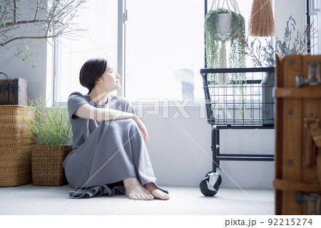 明るい植物のある窓辺の部屋で座って空を見上げて休憩する日本人女性 92215274