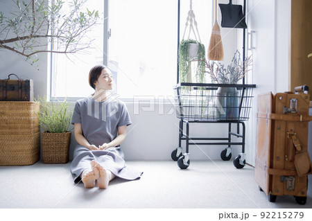 明るい植物のある窓辺の部屋で座って空を見上げて休憩する日本人女性 92215279