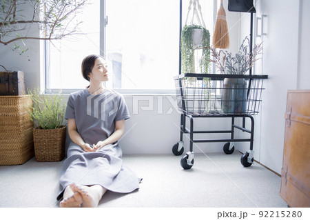 明るい植物のある窓辺の部屋で座って空を見上げて休憩する日本人女性 92215280