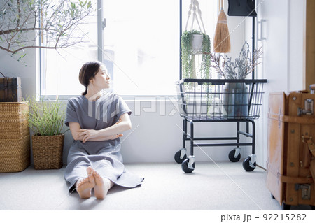 明るい植物のある窓辺の部屋で座って空を見上げて休憩する日本人女性 92215282