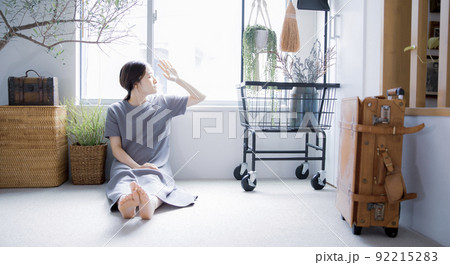 明るい植物のある窓辺の部屋で座って空を見上げて休憩する日本人女性 92215283