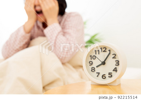 パジャマを着て寝室で寝るミドル女性と目覚まし時計 92215514