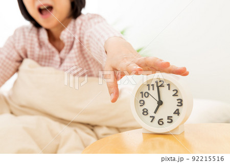 パジャマを着て寝室で寝るミドル女性と目覚まし時計 92215516