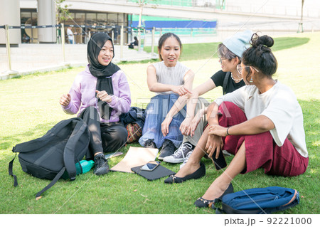 Group of young Asian women sitting on green lawn and chatting. 92221000