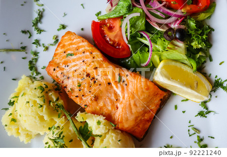 Baked salmon with mash potato, lemon, tomatoes, red onions, olives and salad leaves on white background 92221240