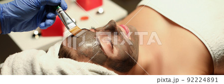 Spa centre worker applying clay mask on clients face with special tool 92224891