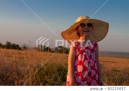 Adorable little girl straw hat pink summer dress with spikelets in hand in wheat field back view. Long blonde hair child 92225057