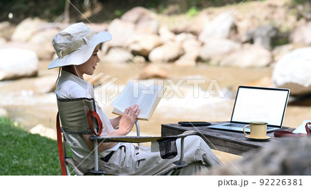 Calm female traveler reading book, enjoying camping alone near the river bank. Adventure, travel and camping concept 92226381