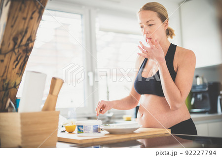 Beautiful sporty fit young pregnant woman preparing healthy meal in home kitchen. Healty lifestyle concept. Beautiful sporty fit young pregnant woman preparing healthy meal in home kitchen. Healty lifestyle concept. 92227794