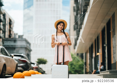 Portrait of young woman with suitcase and looking at camera 92230536