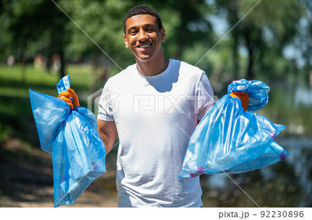 Guy holding trash bags smiling confidently at camera Guy holding trash bags smiling confidently at camera 92230896