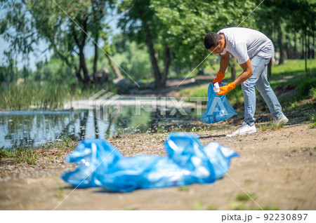 Guy picking up trash in bag near pond Guy picking up trash in bag near pond 92230897