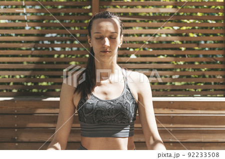 A woman meditates in the lotus position and relaxes in nature in the park in summer sunny weather. Yoga, mental health, relaxation, health concept. 92233508