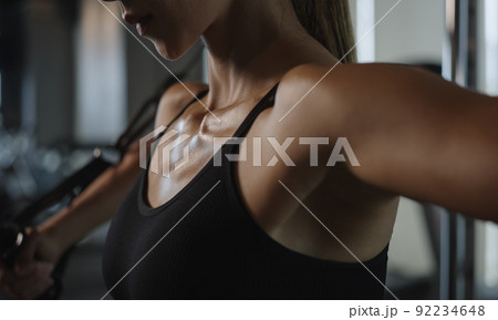 Sporty woman exercising on multistation at gym for arm and shoulders muscles. Fitness exercising in gym. 92234648