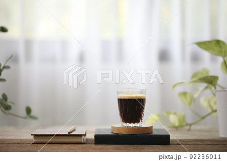 Coffee with crema in a aglass cup and notebooks on wooden table with plants Coffee with crema in a aglass cup and notebooks on wooden table with plants 92236011