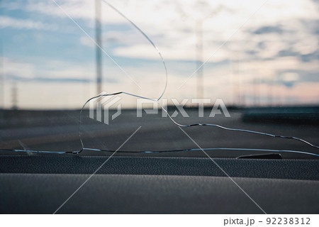 Cracks on car windshield glass hit by stone ejected from under the wheels of another car 92238312