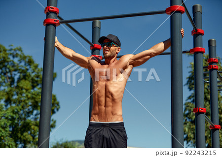 Athletic sportsman trains on the horizontal bars. Training at the open air sprorts ground. Athletic sportsman trains on the horizontal bars. Training at the open air sprorts ground. 92243215