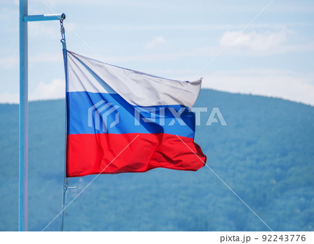 The Russian flag flutters against the blue sky and hills 92243776