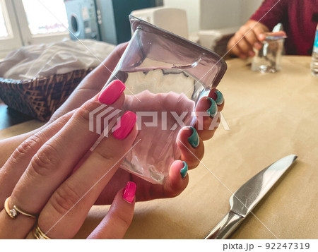 girl with gold rings on her fingers and bright manicure. blue and pink nails. in the hands of a girl a transparent glass with clean, drinking water 92247319