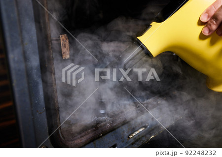 Experienced worker in rubber gloves steam-cleaning kitchen equipment. 92248232