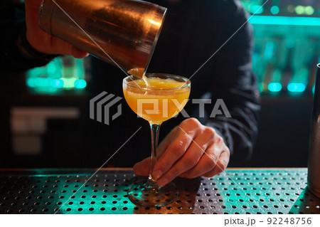 Barman in shirt and apron making an alcoholic drink with ice in a cocktail glass. 92248756