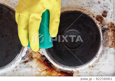 hand in household glove cleaning grease and dirt from kitchen stove 92256061