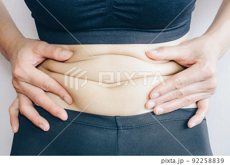 Close-up of Woman touching her fat belly, woman's hand holding excessive belly fat. Being overweight is one of the leading causes of major diseases such as heart disease, stroke, high blood pressure. Close-up of Woman touching her fat belly, woman's hand holding excessive belly fat. Being overweight is one of the leading causes of major diseases such as heart disease, stroke, high blood pressure. 92258839