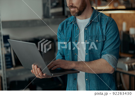 Unrecognizable man processes orders on a laptop while working in a repair shop Unrecognizable man processes orders on a laptop while working in a repair shop 92263430