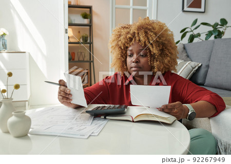 African girl sitting at table in living room and calculating her bills, she paying bills for rent, gas and electricity African girl sitting at table in living room and calculating her bills, she paying bills for rent, gas and electricity 92267949