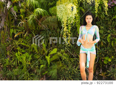 Young 20s Asian slim Woman sit and fashion poses in green forest tree wall beautiful style bikini 92273100